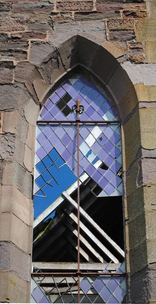 A broken stained-glass window set into a brick wall.